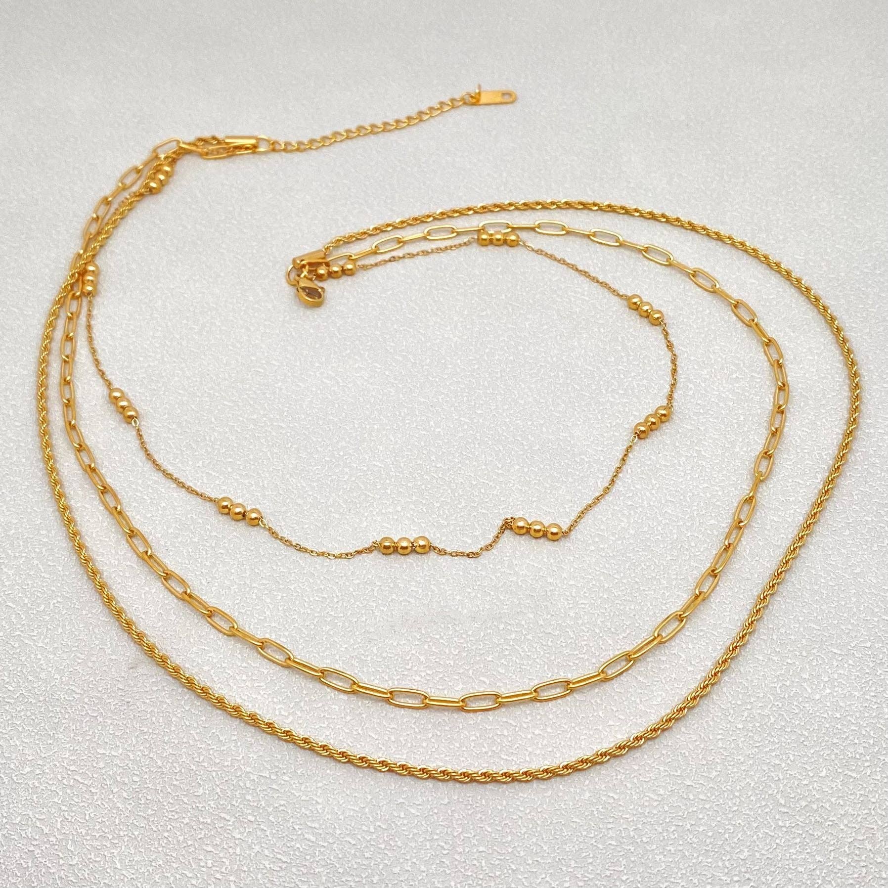 Three gold necklaces of different styles on a light gray background