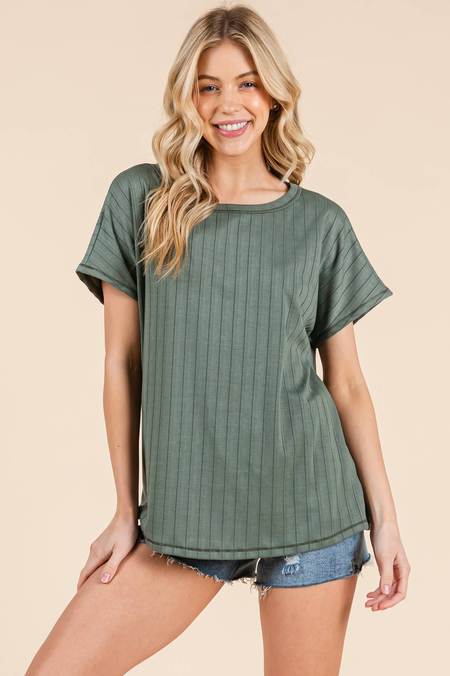 Woman wearing a sage green ribbed t-shirt and denim shorts on a beige background