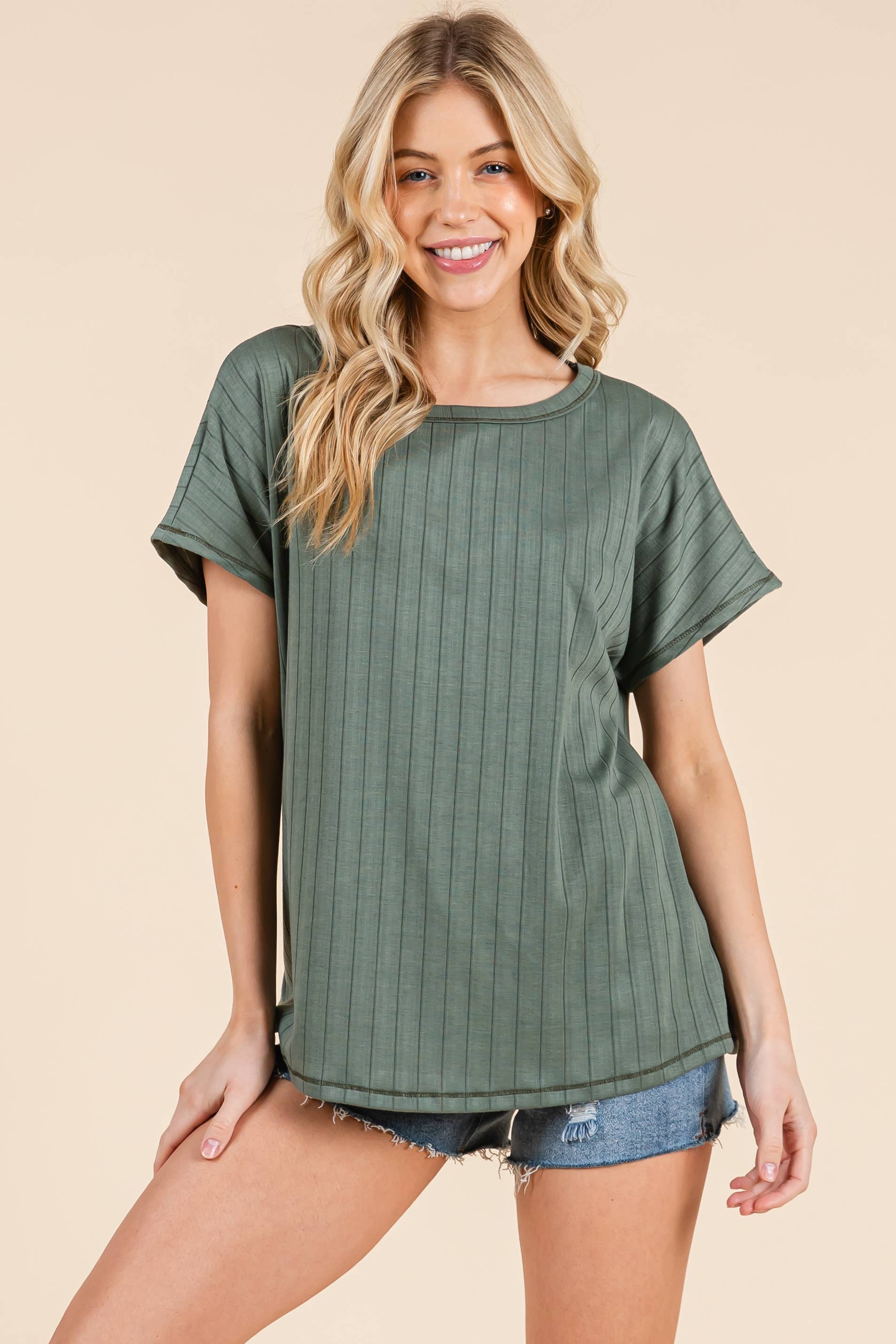 Woman wearing a sage green ribbed t-shirt and denim shorts on a beige background
