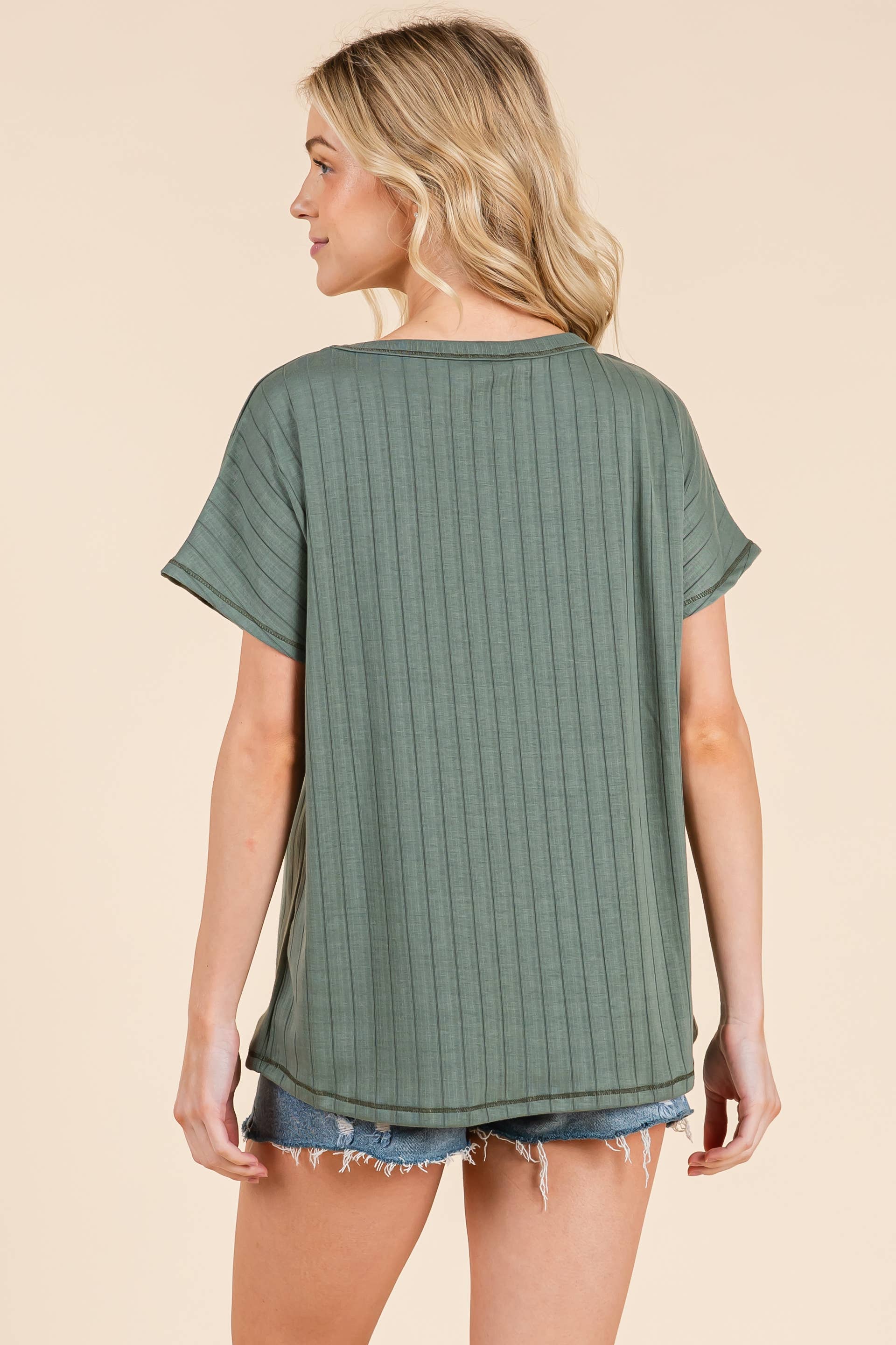 the back of a Woman wearing a  sage green ribbed t-shirt and denim shorts on a beige background