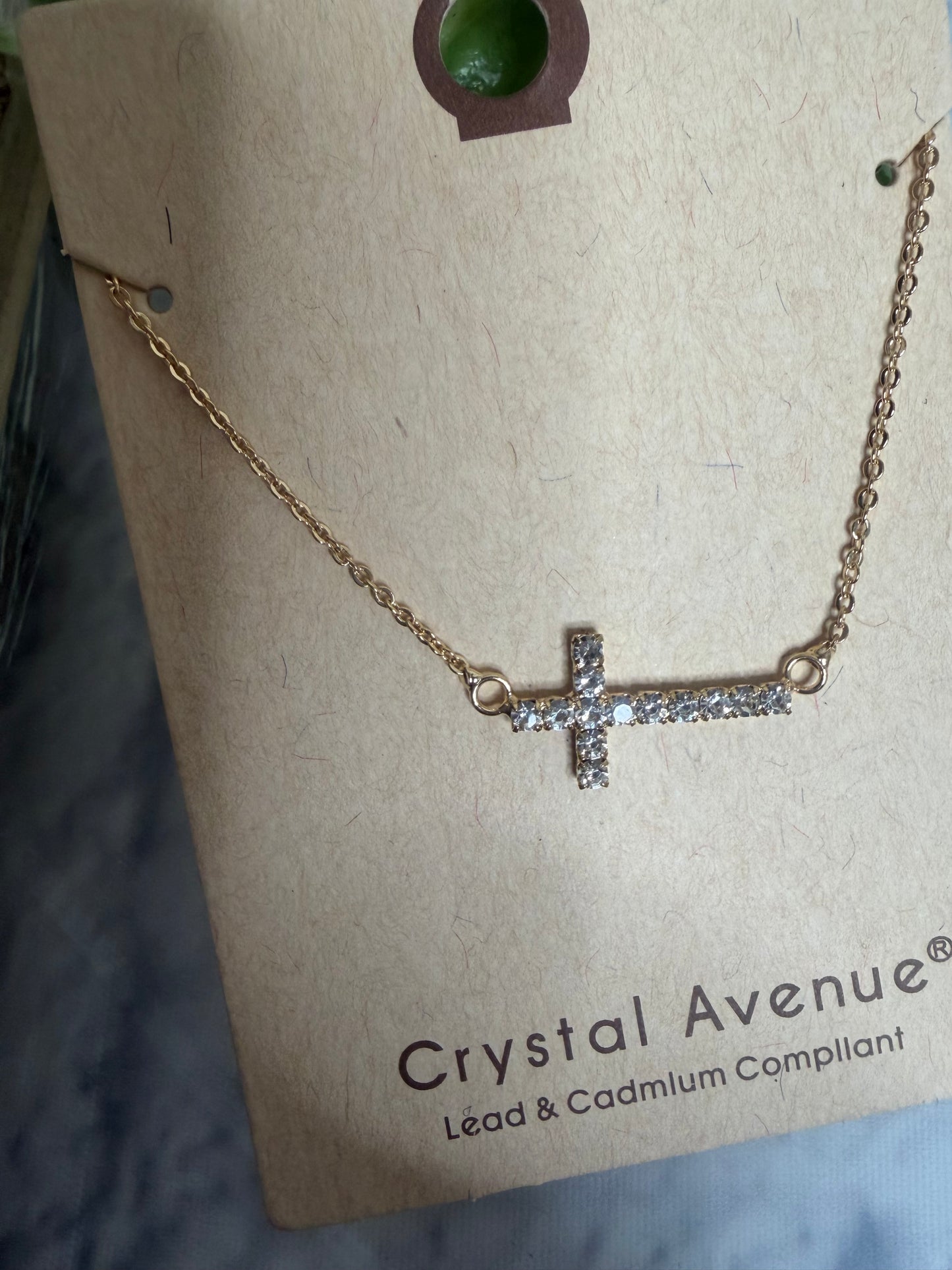 Gold necklace with a cross pendant on a 'Crystal Avenue' branded card.