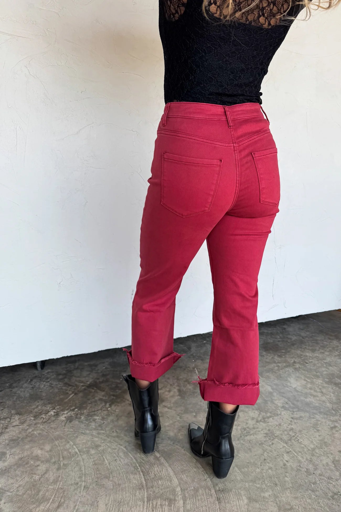 Person wearing maroon pants and black boots standing against a white wall.